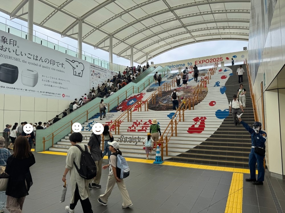 夢洲駅から万博会場に向かう階段・エスカレーターの様子。大勢の人々が会場方面に向かっている。